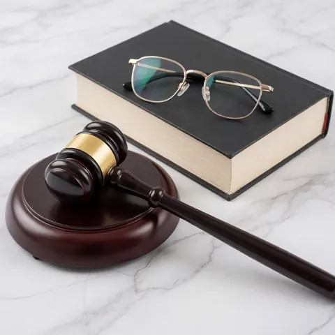 Un marteau de juge, un livre et des lunettes reposent sur une surface en marbre blanc et gris.