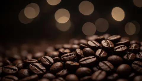 Gros plan sur des grains de café torréfiés posés sur une surface sombre, créant un arrière-plan abstrait et flou avec des lumières chaleureuses.