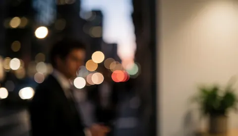 Un homme d'affaires debout près d'une fenêtre avec des lumières bokeh de la ville au coucher du soleil.