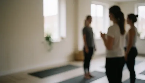 Groupe de personnes lors d'un cours de yoga dans un studio avec des couvertures et des fenêtres, image floue mettant en valeur la lumière naturelle.