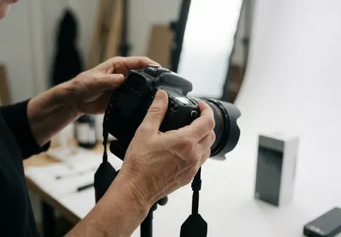 Une main ajuste une caméra reflex avec un objectif large sur fond blanc dans un studio équipé d'éclairage professionnel.