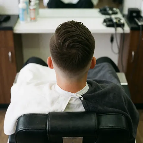 Vue d'une coupe de cheveux avec dégradé réalisée sur une chaise de barbier, accompagnée de serviettes et de produits de soin visibles, sous un éclairage clair et net.