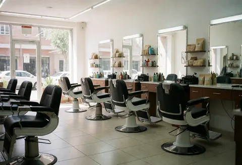 Intérieur d'une salle de barbier moderne équipée de chaises noires, de miroirs et d'étagères contenant des produits de soin.