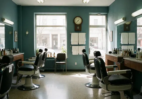 Intérieur d'un salon de barbier avec des murs bleu-vert, des chaises de barbier, des fenêtres laissant entrer la lumière naturelle et des serviettes blanches suspendues.