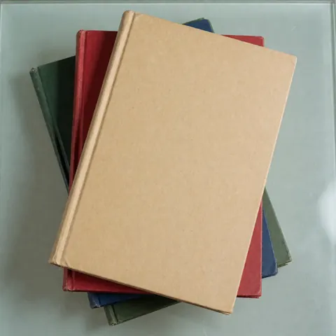 Vue de dessus d'une pile de livres aux couvertures colorées posée sur une surface en verre transparente, évoquant l'univers académique.