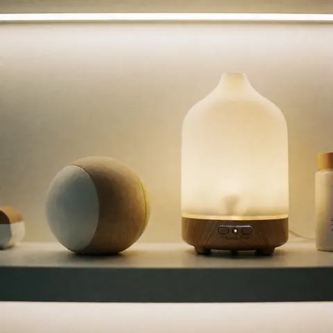 Un diffuseur d'arômes et des objets décoratifs disposés sur une étagère en bois éclairée par une lumière chaude, créant une ambiance apaisante.