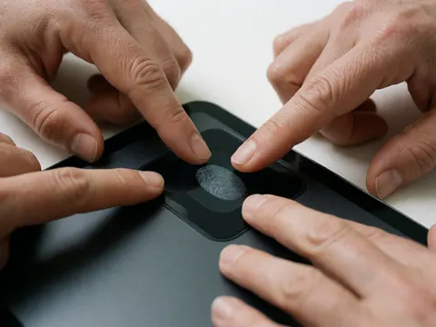 Deux mains posent des doigts sur un lecteur d'empreintes digitales intégré à une tablette noire placée sur une surface blanche.