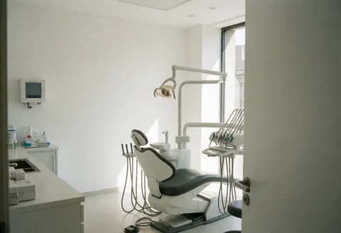 Intérieur d'une clinique dentaire avec chaise, lumière chirurgicale et équipements médicaux sur fond blanc ordonné.