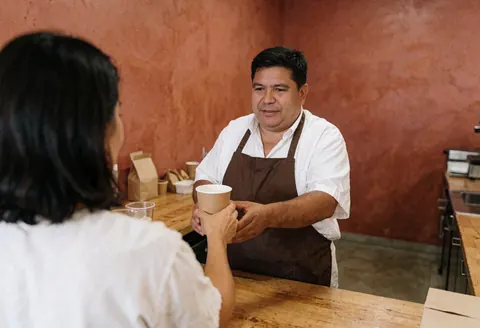 Un employé de café remet une boisson dans un gobelet en papier à une cliente au comptoir.