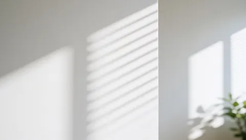 La lumière du soleil traverse les stores et crée des motifs d'ombres nettes sur une surface murale intérieure blanche et lisse.