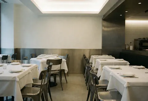 Tables avec nappes blanches et couverts prêts à servir dans un restaurant moderne avec chaises métalliques.