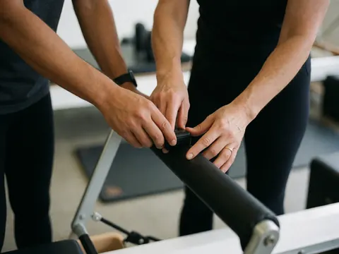 Deux personnes ajustent la tension des ressorts d'un appareil de reformer dans un studio de yoga et pilates.