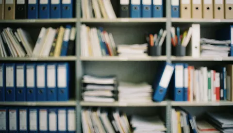 Étagère de bureau contenant des dossiers et des documents bien rangés, servant de fond neutre pour tout type d'activité commerciale ou professionnelle.