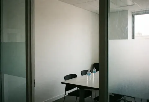 Salle de réunion minimaliste vide avec une table blanche et des chaises noires, deux bouteilles d'eau posées sur la table.