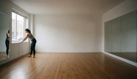 Une femme réalise des étirements près d'une fenêtre dans un studio de pilates aux sols en bois et aux murs vitrés.