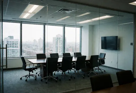 Salle de réunion vide équipée de tables et chaises noires, offrant une vue panoramique sur la ville à travers de grandes baies vitrées.