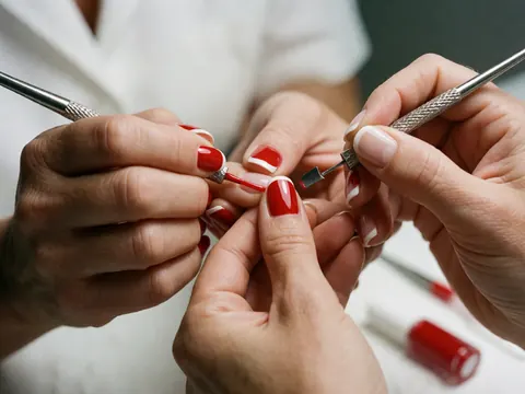 Gros plan d'une manucière utilisant des outils pour appliquer du vernis rouge sur des ongles avec une finition française, montrant le soin et la précision du travail.