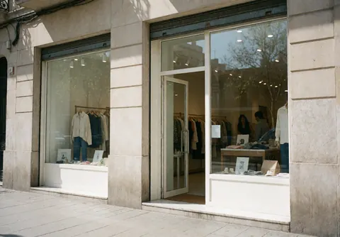 Entrée ouverte d'une boutique de mode moderne avec vitrine exposant des vêtements sur cintres et mannequins.