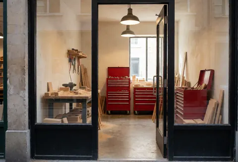 Vue extérieure de la devanture d'un atelier de charpente montrant des outils et des boîtes rouges à travers une porte vitrée.