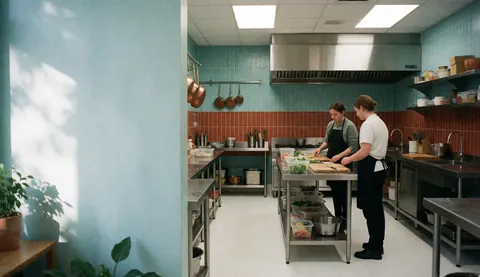 Deux femmes coupant des légumes frais sur une table de travail métallique dans une cuisine professionnelle.
