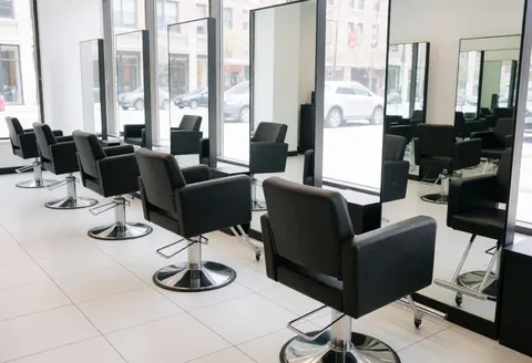 Chaises noires avec base métallique dans un salon moderne équipé de miroirs et de fenêtres.