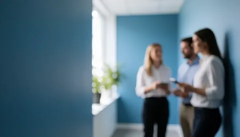 Trois collègues en tenue professionnelle échangent des informations dans un couloir aux murs bleus, l'un tenant un téléphone et l'autre une tablette.