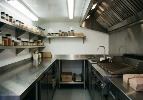 Intérieur d'une cuisine mobile avec plaque de cuisson, grille, étagères à épices et surfaces en acier inoxydable.