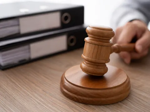 Marteau de juge posé sur un bureau avec des dossiers juridiques et la main d'un avocat en arrière-plan.