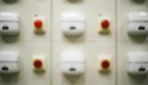 Vue rapprochée d'un panneau de contrôle industriel comportant des interrupteurs et boutons d'alarme rouges et blancs pour la sécurité en entreprise.