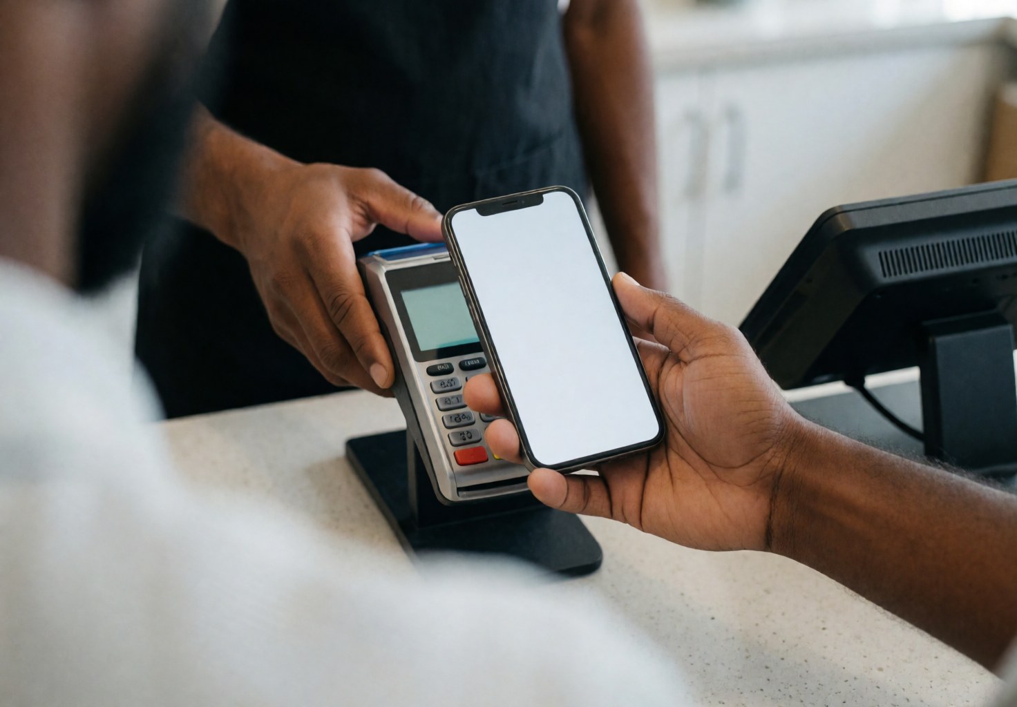 Un client utilise son smartphone pour payer en caisse tandis qu'un employé tient le terminal de paiement sans contact.