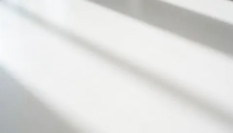 Surface blanche lisse avec des ombres douces de lumière naturelle, idéale pour créer des arrière-plans minimalistes et épurés.