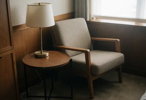 Une chaise en tissu et bois à côté d'une table ronde avec une lampe sur pied dans une pièce aux murs en bois.