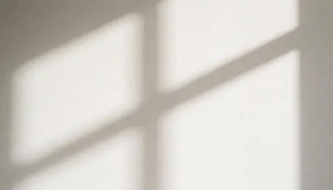 Projection d'une ombre géométrique de stores sur un mur blanc créant un motif lumineux et sombre pour fond neutre.