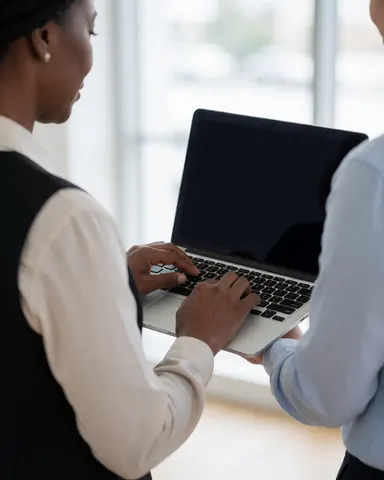 Un homme et une femme travaillent ensemble sur un ordinateur portable dans un bureau moderne baigné de lumière naturelle.