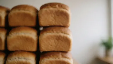 Miche de pain frais cuit empilée avec une texture dorée et douce, vue rapprochée sur fond flou.