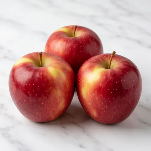 Vue rapprochée de trois pommes rouges luisantes posées sur une surface en marbre blanc poli, évoquant la fraîcheur et la qualité des produits alimentaires.