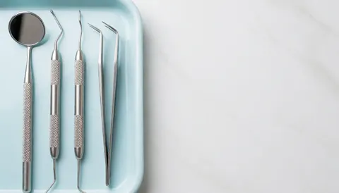 Des instruments dentaux en acier inoxydable disposés sur un plateau bleu posé sur une surface en marbre blanc.