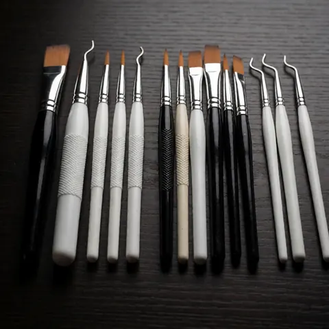 Vue rapprochée d'un ensemble d'outils de manucure et de pédicure, pinceaux et pinces, disposés sur une table en bois sombre.