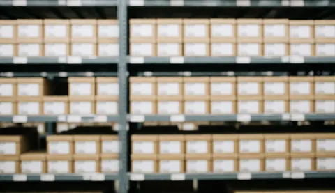 Des étagères métalliques remplies de boîtes en carton dans un entrepôt logistique, offrant un fond neutre pour du texte.