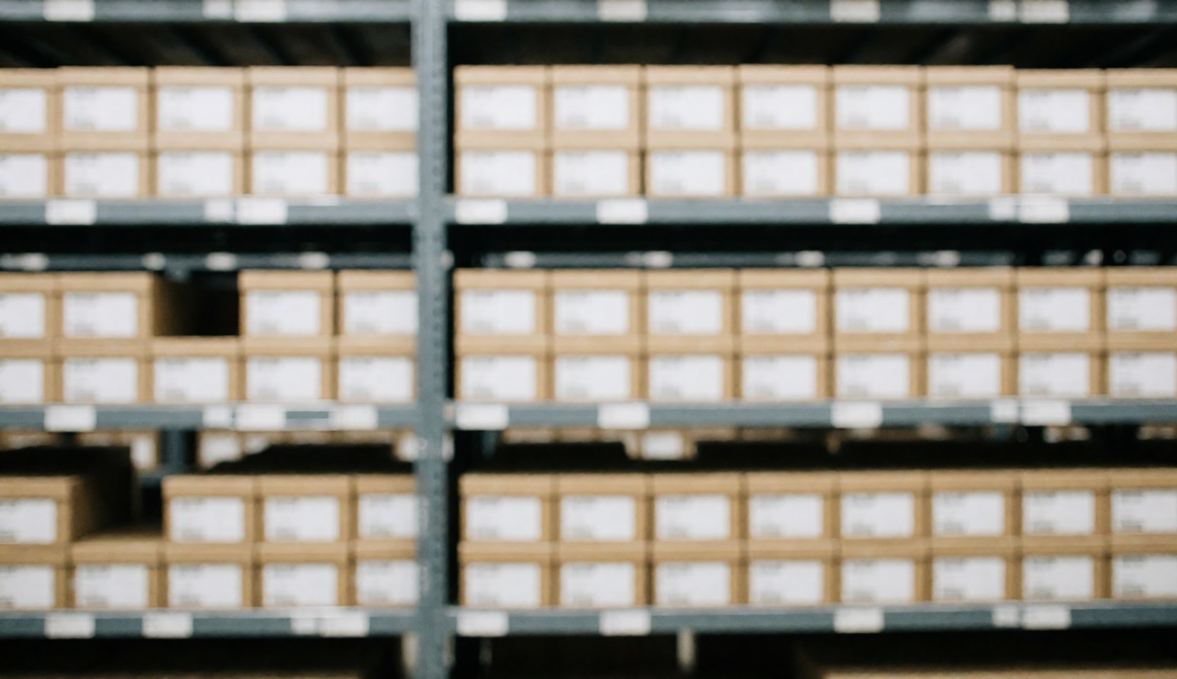 Des étagères métalliques remplies de boîtes en carton dans un entrepôt logistique, offrant un fond neutre pour du texte.