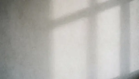 Mur en béton texturé éclairé par la lumière naturelle créant des ombres douces dans un intérieur minimaliste.