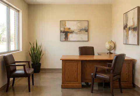 Intérieur d'une réception professionnelle avec bureau en bois, chaises, plante verte et cadres au mur, éclairée et vide.