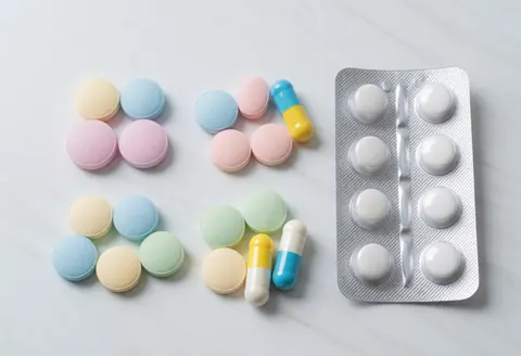 Diverses pastilles et capsules colorées disposées sur une surface blanche, incluant un blister contenant des comprimés blancs.