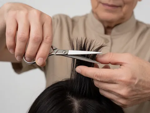 Un coiffeur coupe les cheveux d'une cliente à l'aide de ciseaux professionnels dans un salon de coiffure.