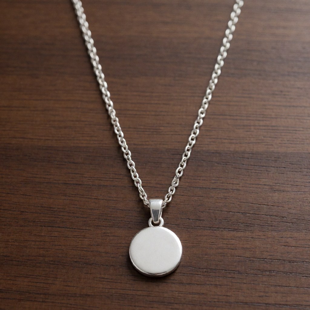 Collier en argent avec un pendentif circulaire posé sur une table en bois, vue de dessus.