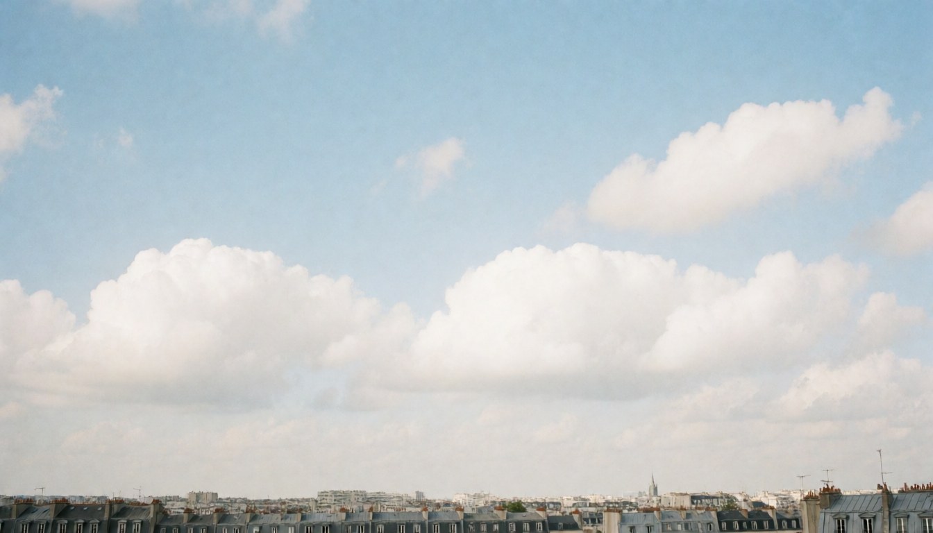 Vue d'un ciel bleu parsemé de nuages blancs au-dessus des toits d'une ville européenne, offrant un fond urbain minimaliste et épuré.