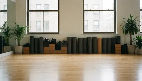 Intérieur d'un studio de yoga désert avec sols en bois, tapis roulés, plantes vertes et blocs, éclairé par la lumière du jour entrant par les fenêtres.