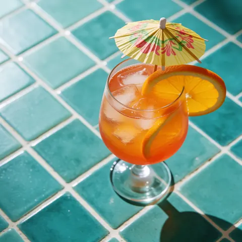Cocktail tropical garni de citron et d'un petit parapluie dans un verre posé sur des carreaux turquoise.