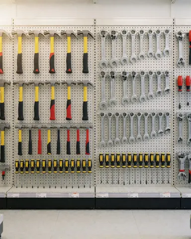 Divers outils tels que marteaux, clés et tournevis accrochés sur un mur perforé dans un magasin de quincaillerie.