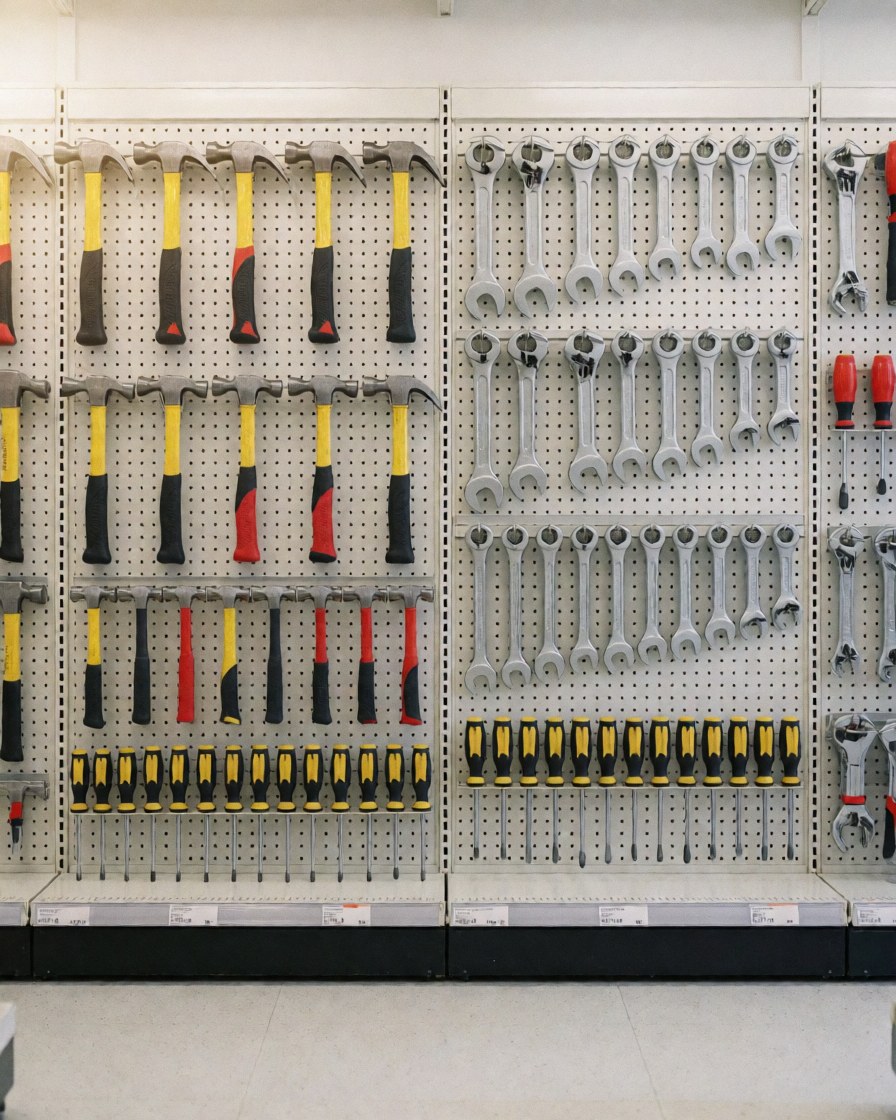 Divers outils tels que marteaux, clés et tournevis accrochés sur un mur perforé dans un magasin de quincaillerie.